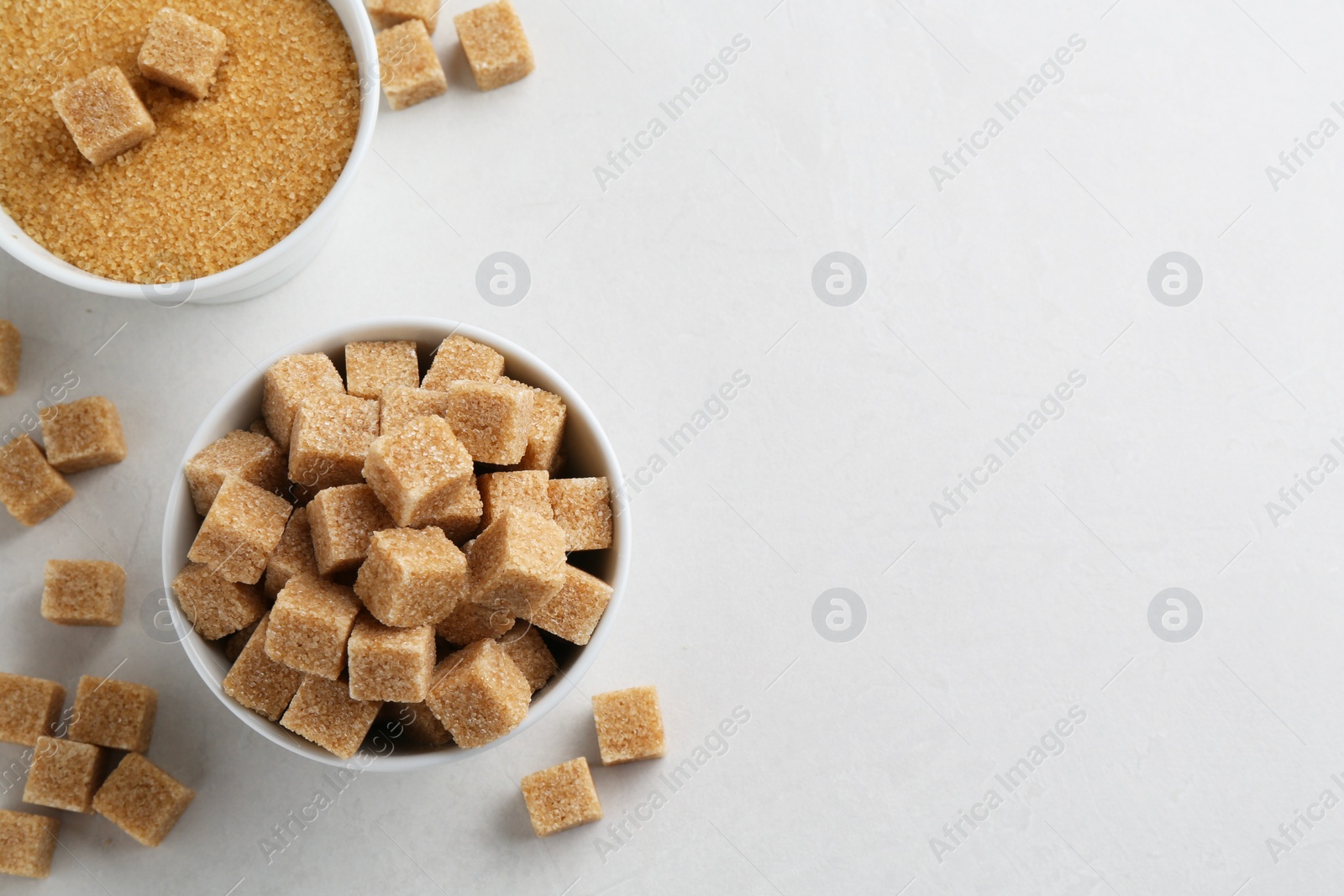 Photo of Brown granulated sugar and cubes on white textured table, flat lay. Space for text