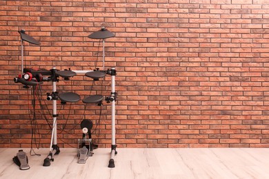 Photo of Modern electronic drum kit near red brick wall indoors, space for text. Musical instrument