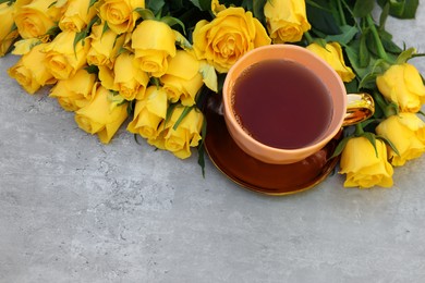 Cup of tea and beautiful yellow roses on light table, above view. Space for text