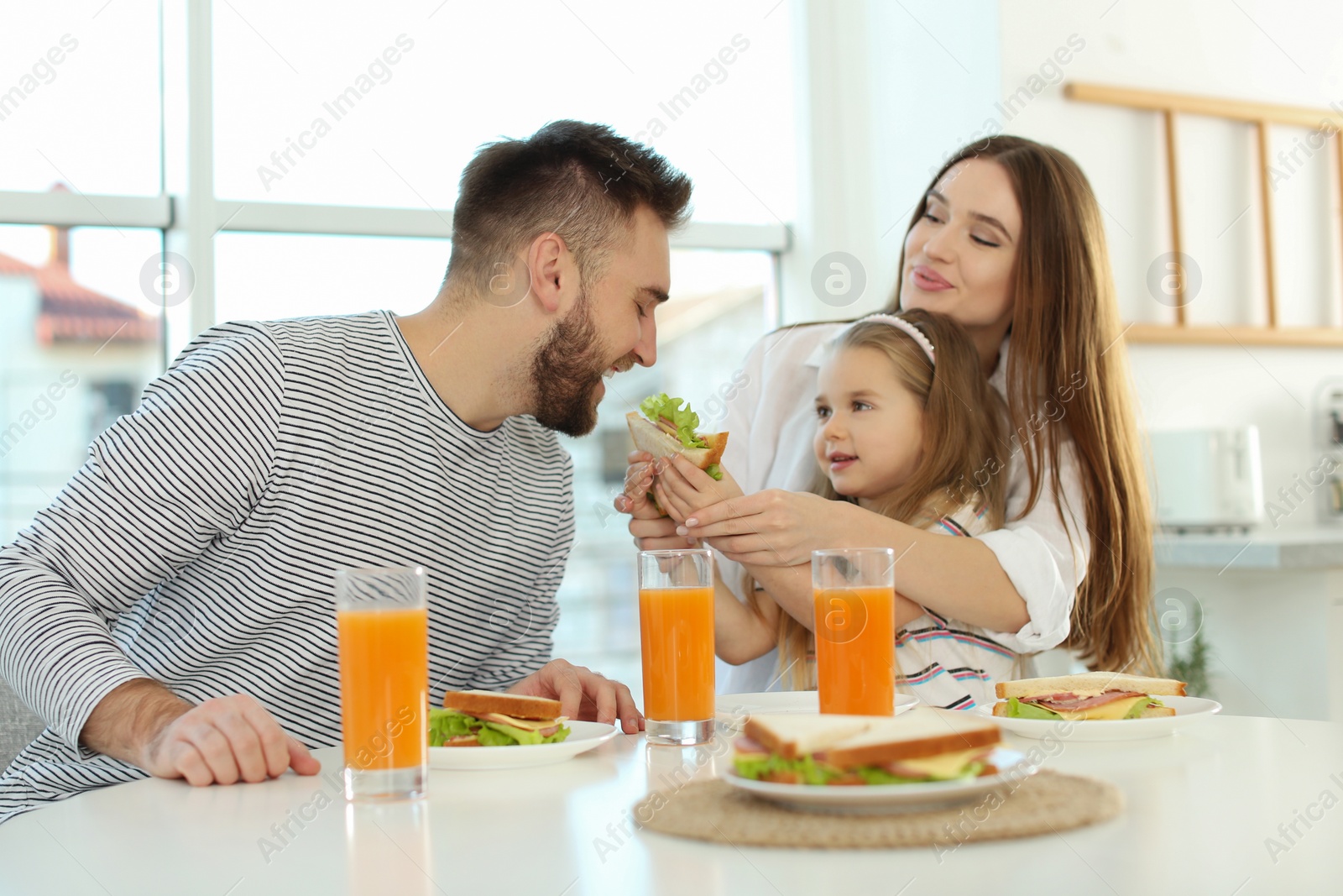 Photo of Happy family having breakfast with sandwiches at table in kitchen