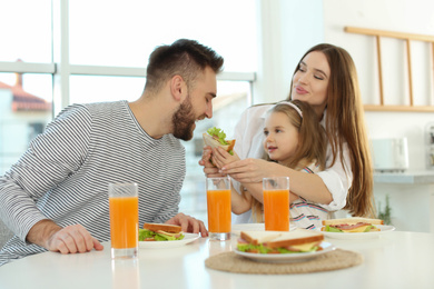 Photo of Happy family having breakfast with sandwiches at table in kitchen