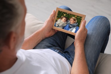 Senior man holding frame with photo of his family at home, closeup
