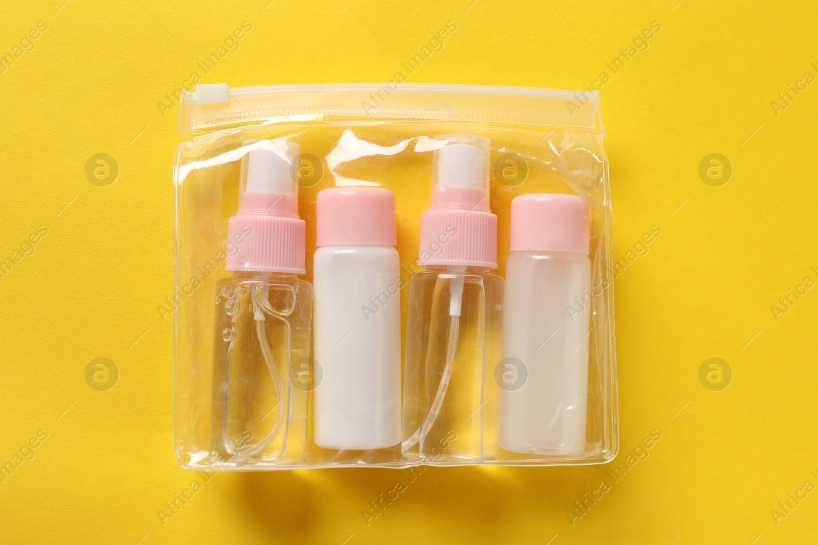 Photo of Cosmetic travel kit in plastic bag on yellow background, top view. Bath accessories