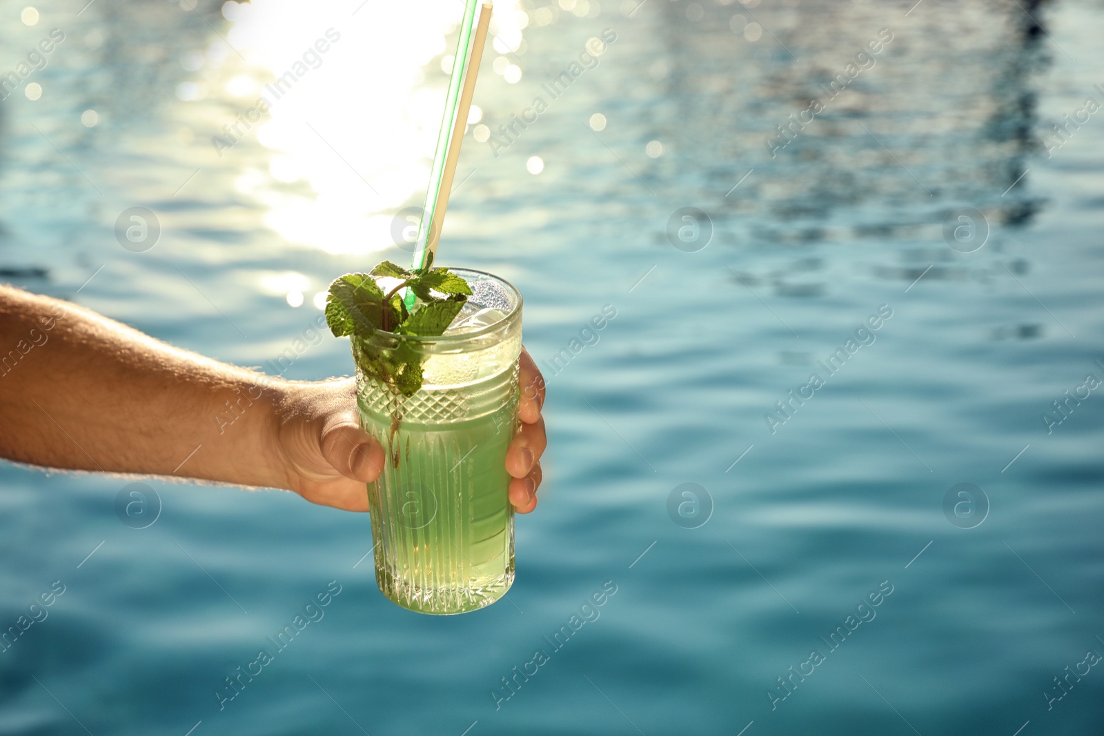 Photo of Man with glass of fresh summer cocktail near swimming pool outdoors, closeup. Space for text