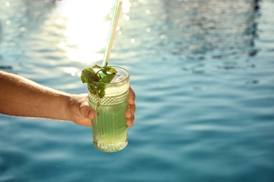 Photo of Man with glass of fresh summer cocktail near swimming pool outdoors, closeup. Space for text
