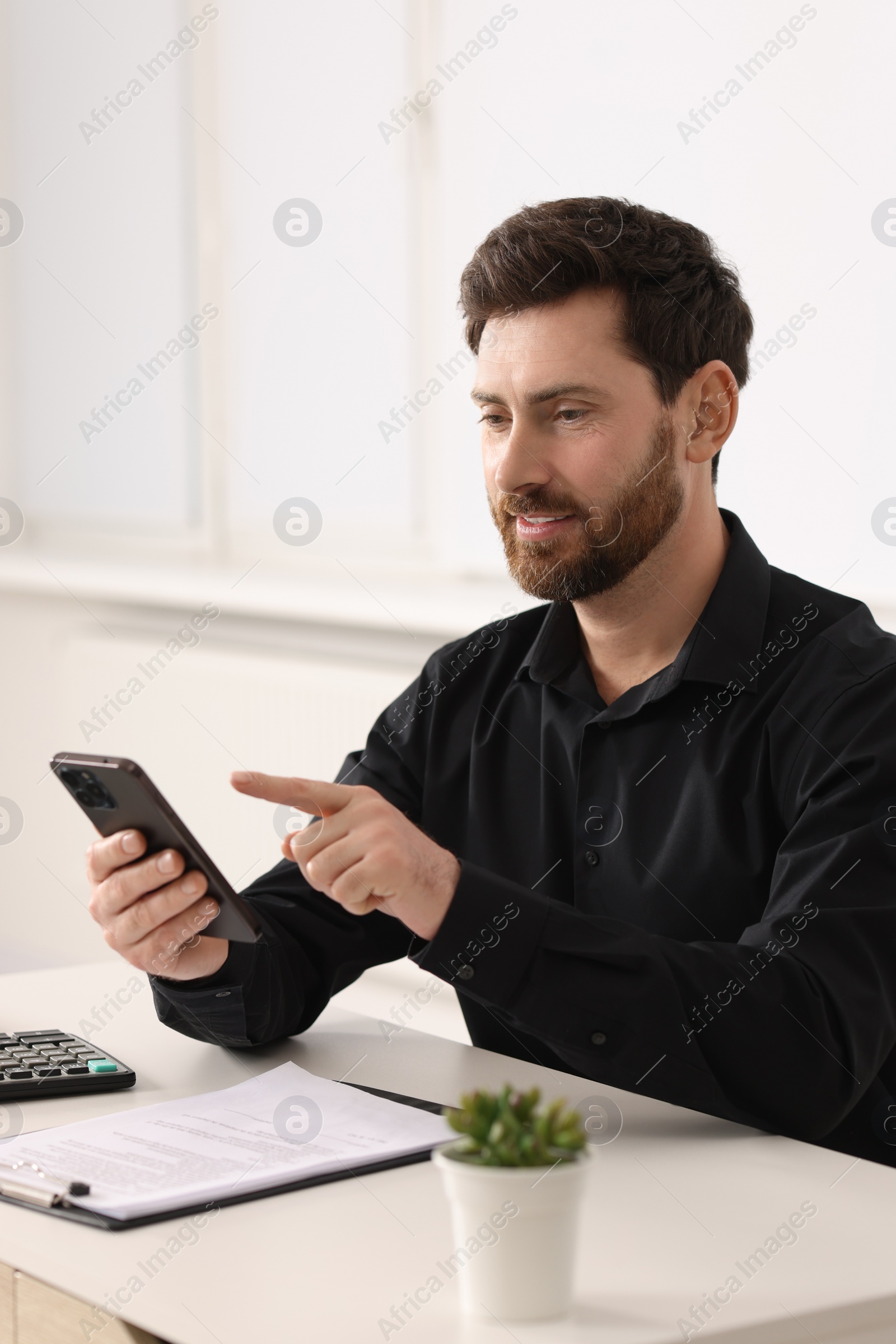 Photo of Smiling man using smartphone at table in office