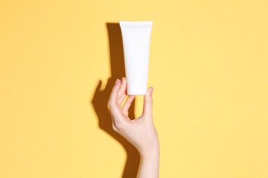 Photo of Woman holding tube of cream on yellow background, closeup