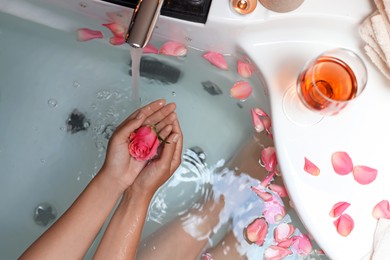 Photo of Woman holding rose flower while taking bath, above view. Romantic atmosphere