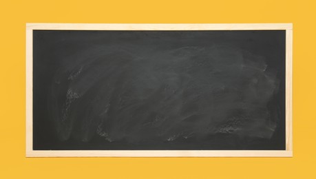 Dirty black chalkboard on orange background. School equipment