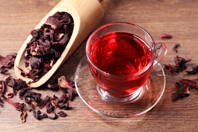 Cup of fresh hibiscus tea and dry flower leaves on wooden table