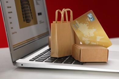 Mini shopping bags, box and credit card on laptop against red background, closeup. Online store