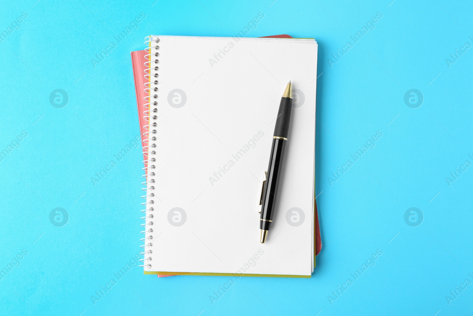 Photo of Notebooks and pen on light blue background, top view