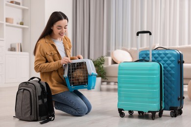 Travelling with pet. Smiling woman looking at carrier with her dog indoors