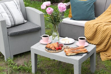 Photo of Morning drink, pastry, berries, cheese and vase with flowers on rattan table. Summer breakfast outdoors