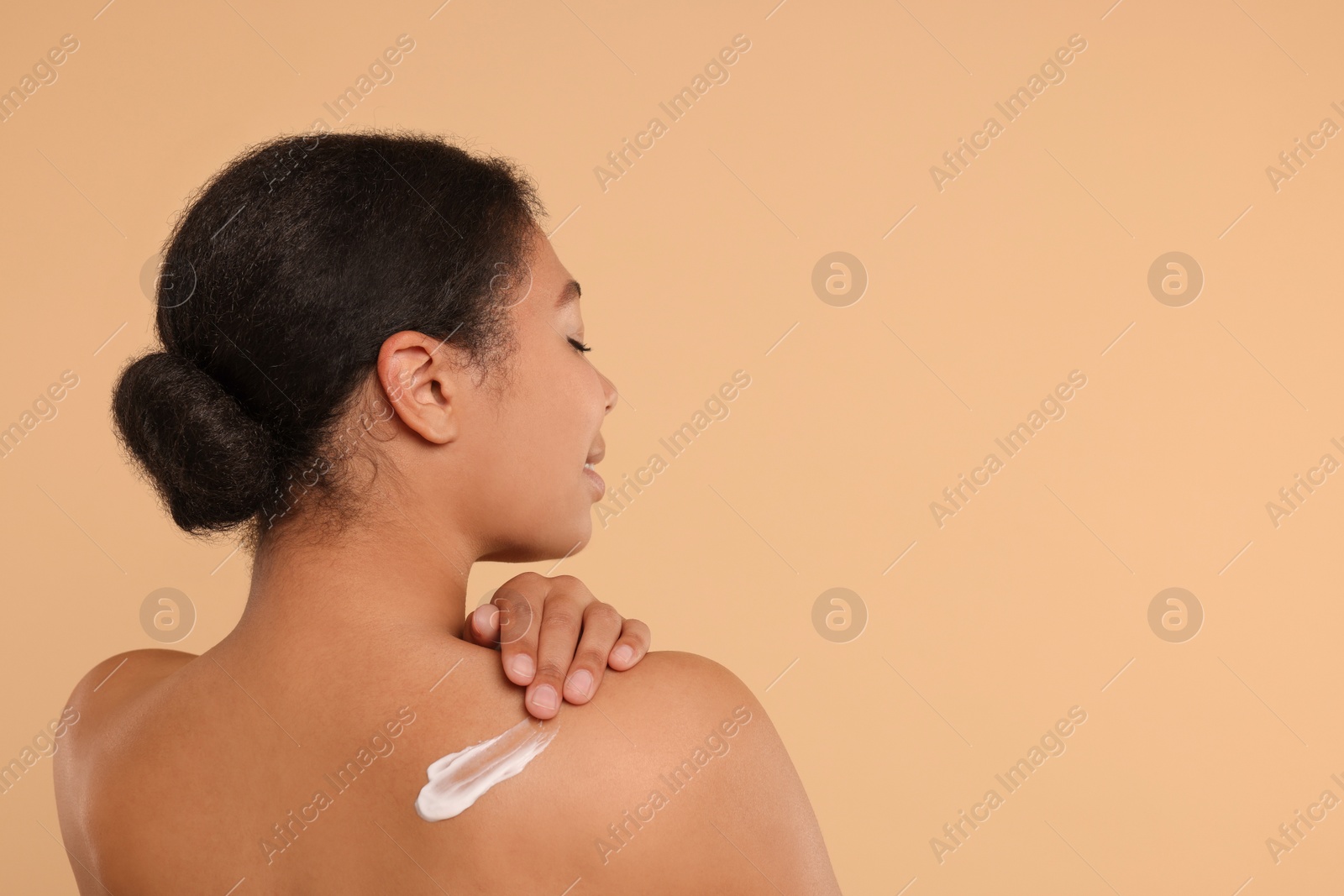 Photo of Young woman applying body cream onto back on beige background. Space for text