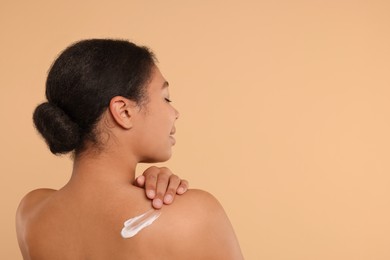 Young woman applying body cream onto back on beige background. Space for text