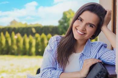 Portrait of beautiful young woman sitting on chair at backyard, space for text