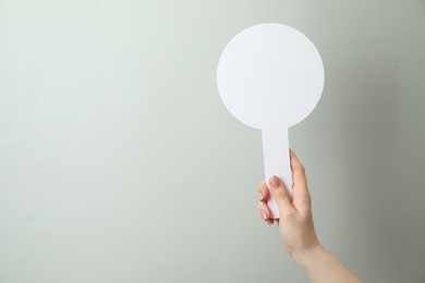 Photo of Woman holding blank auction paddle on light grey background, closeup. Space for text