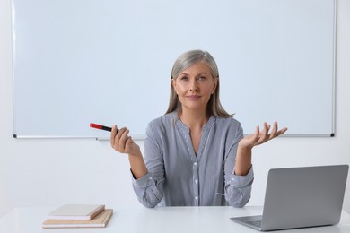 Photo of Professor giving lecture near laptop at desk in classroom