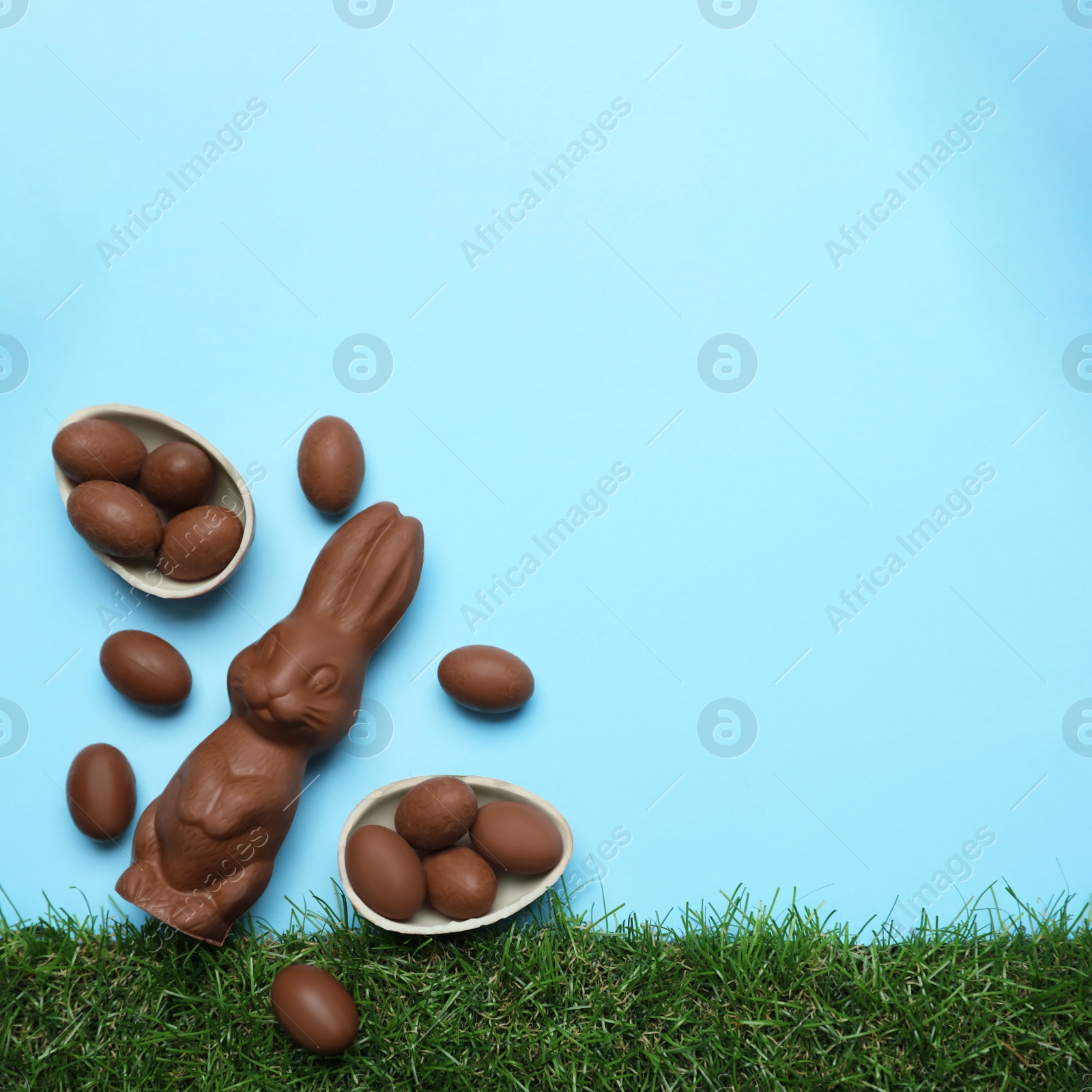 Photo of Chocolate Easter bunny and eggs with green grass on light blue background. Space for text