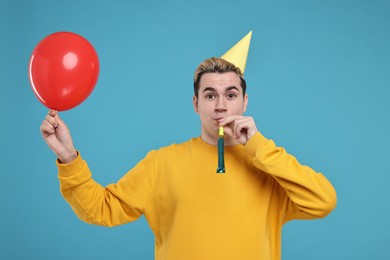 Young man with party hat, blower and balloon on light blue background