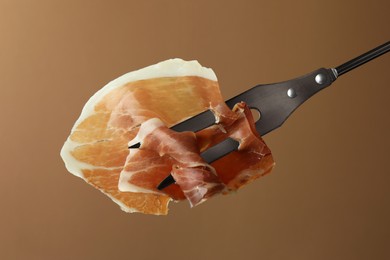 Photo of Fork with slice of tasty jamon on brown background, closeup