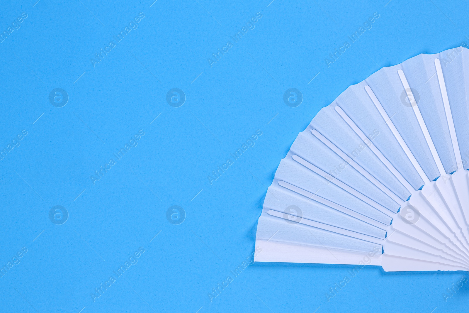 Photo of White hand fan on light blue background, top view. Space for text