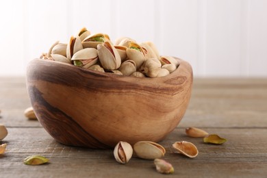 Photo of Tasty pistachios in bowl on wooden table, closeup