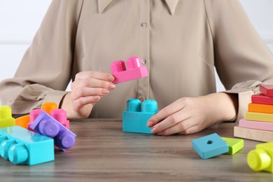 Photo of ABA therapist with colorful building blocks at wooden table, closeup