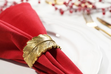 Photo of Red fabric napkin with beautiful decorative ring on white table, closeup