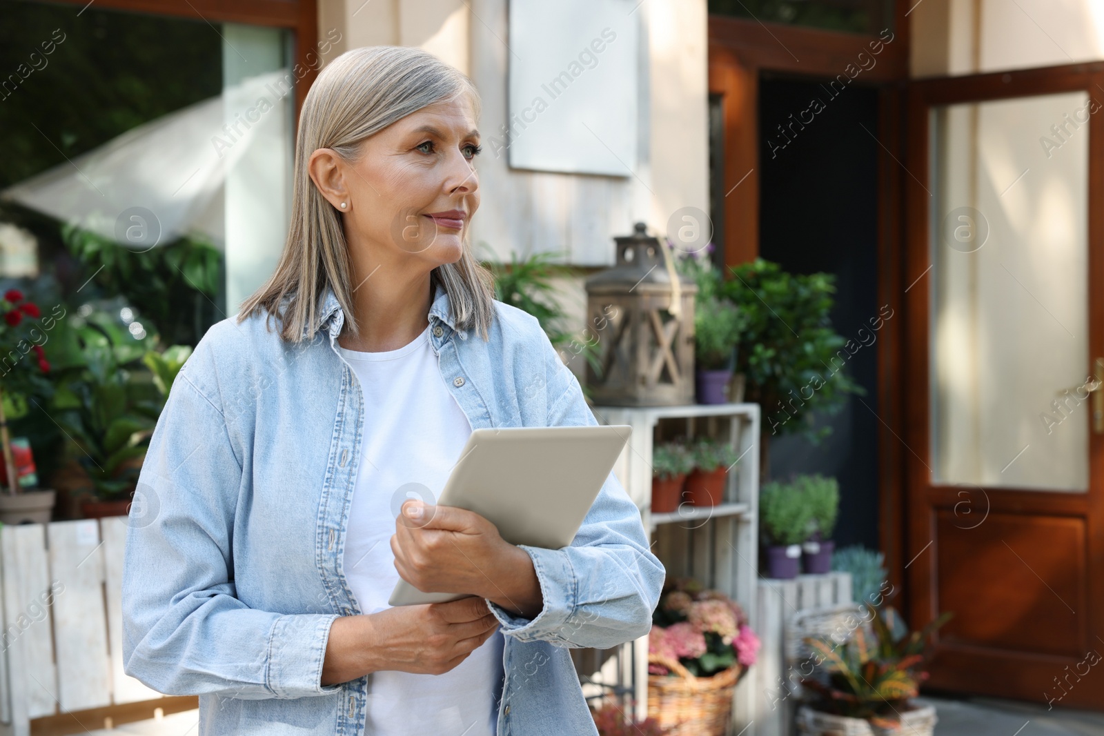 Photo of Beautiful business owner with tablet near her flower shop outdoors, space for text