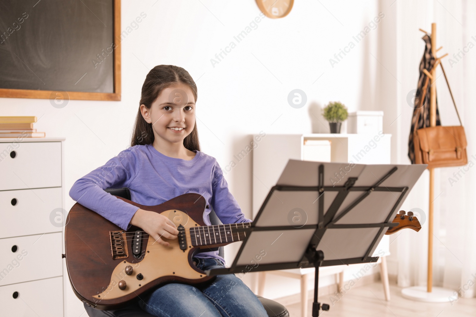 Photo of Little girl playing guitar at music lesson. Learning notes