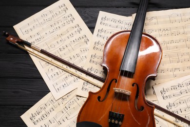 Violin, bow and music sheets on black wooden table, above view