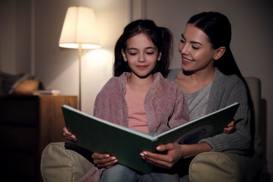 Photo of Little girl with mother reading fairy tale at home in evening
