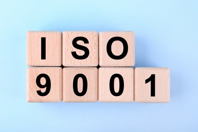 Photo of International Organization for Standardization. Wooden cubes with abbreviation ISO and number 9001 on light blue background, flat lay