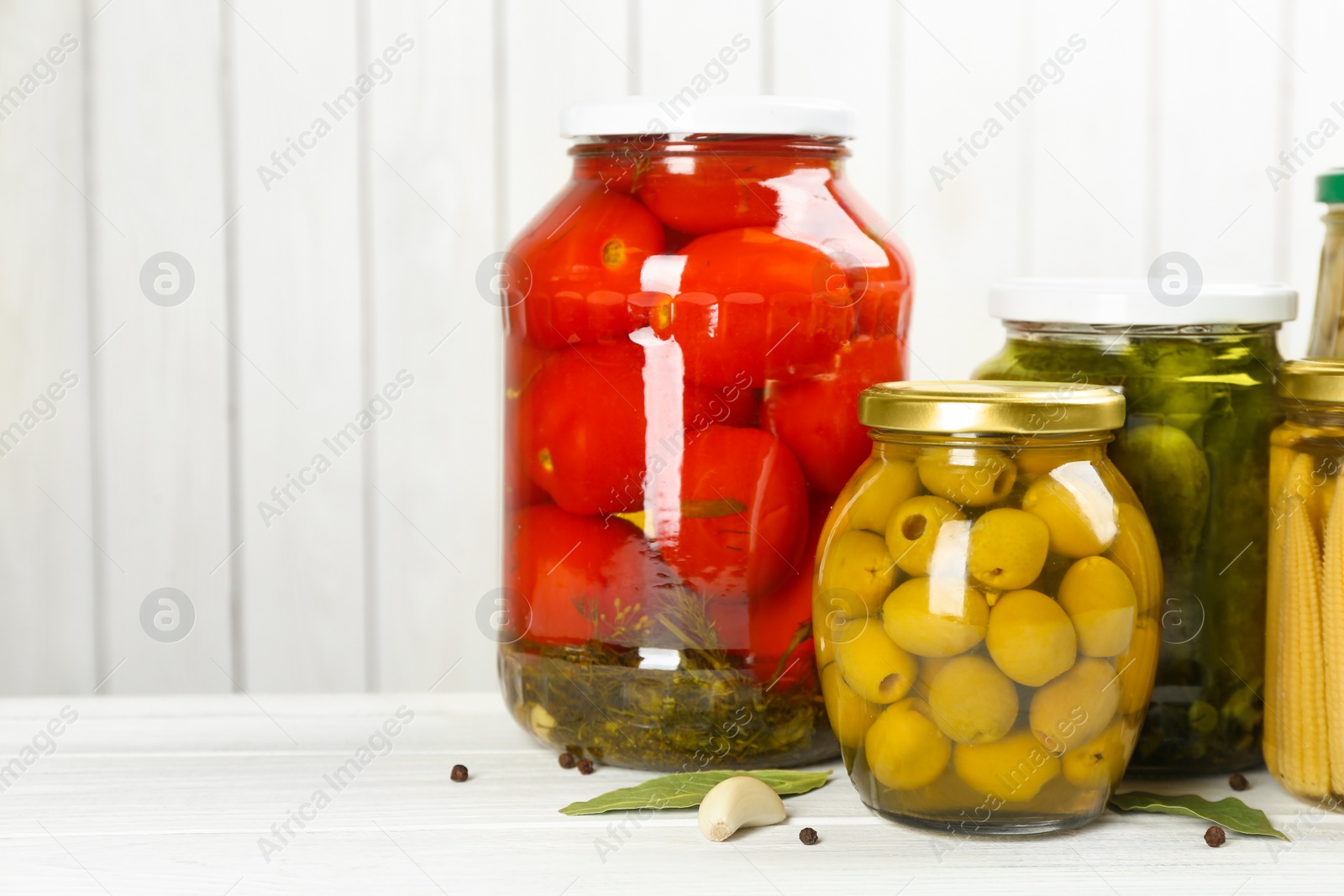 Photo of Glass jars with different pickled vegetables on white wooden background. Space for text