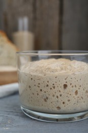 Glass jar with sourdough on grey wooden table, closeup