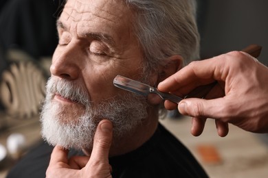 Photo of Professional barber shaving client's beard with blade in barbershop