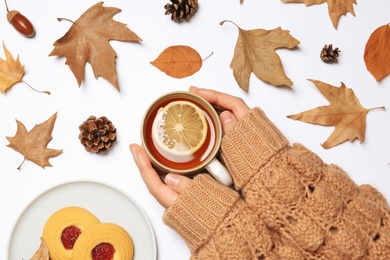 Woman in autumn sweater holding cup of hot cozy drink on white background, top view