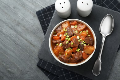 Delicious beef stew with carrots, green onions and potatoes served on grey table, flat lay. Space for text