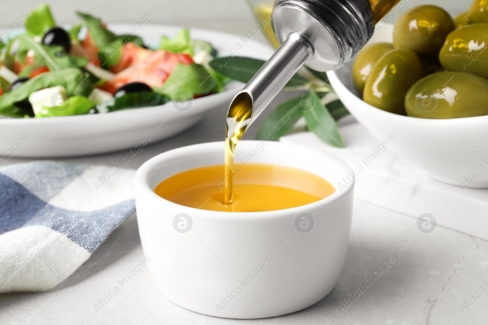 Photo of Pouring cooking oil into bowl on light grey marble table