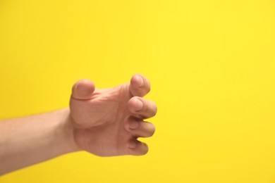 Man holding something in hand on yellow background, closeup. Space for text