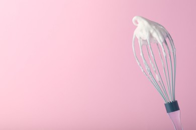 Photo of Whisk with whipped egg whites on pink background, space for text