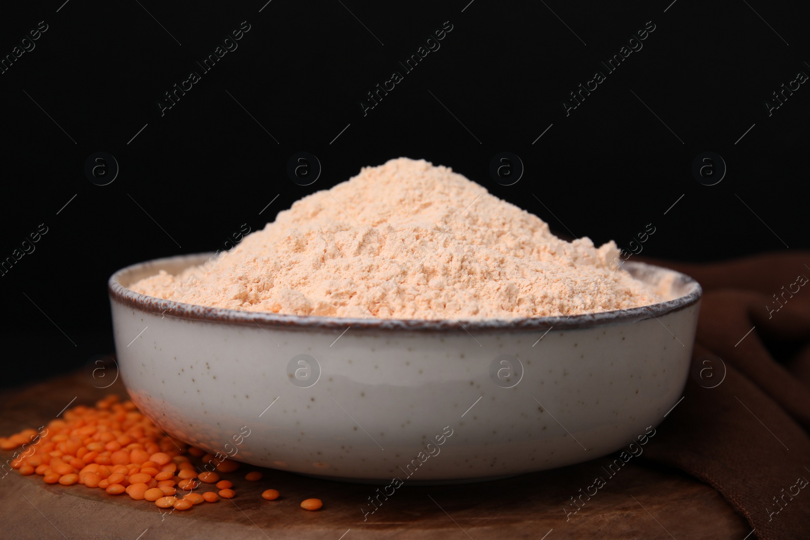 Photo of Bowl of lentil flour and seeds on wooden table against black background