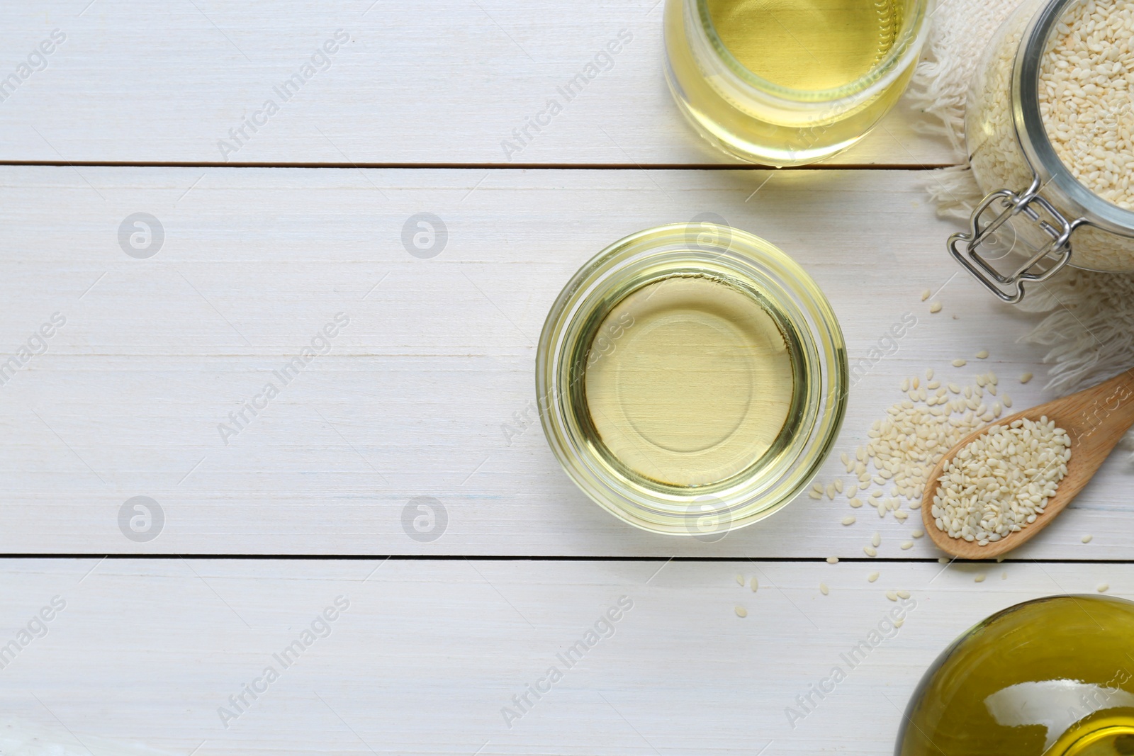 Photo of Jar of organic sesame oil and seeds on white wooden table, flat lay. Space for text