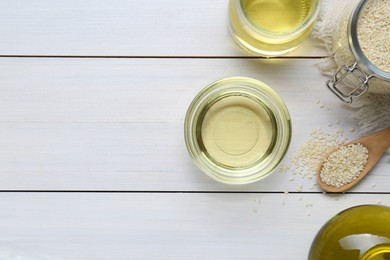 Jar of organic sesame oil and seeds on white wooden table, flat lay. Space for text