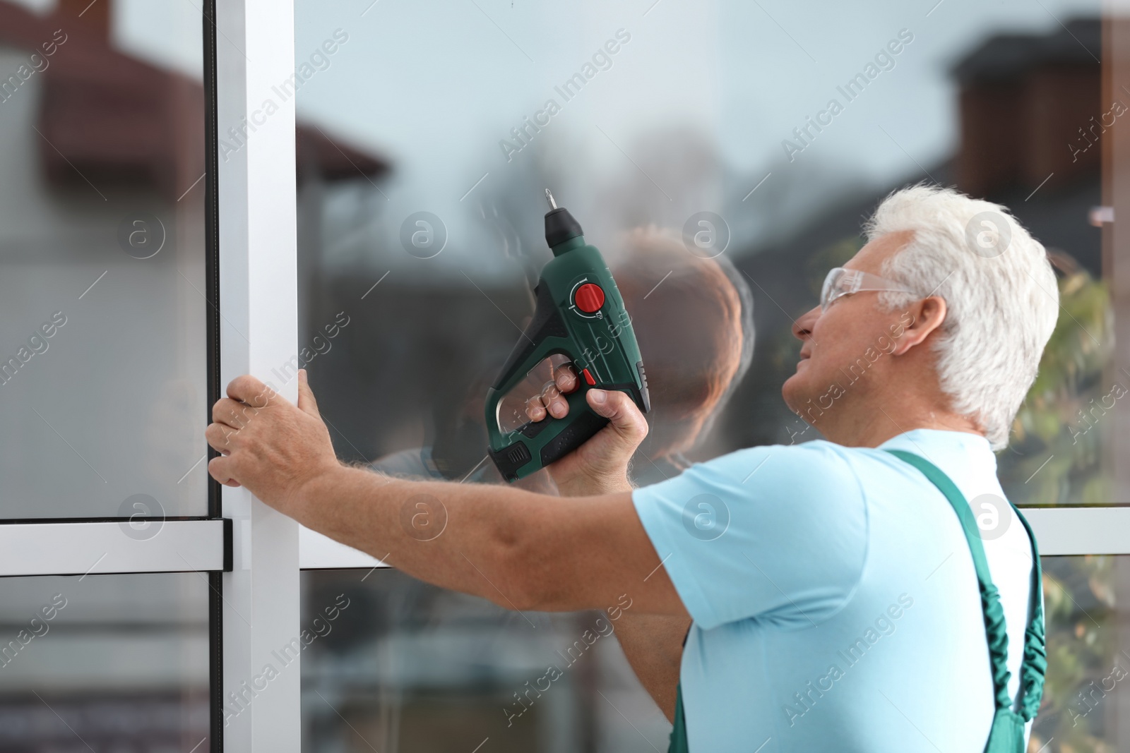 Photo of Mature construction worker repairing plastic window with electric screwdriver indoors