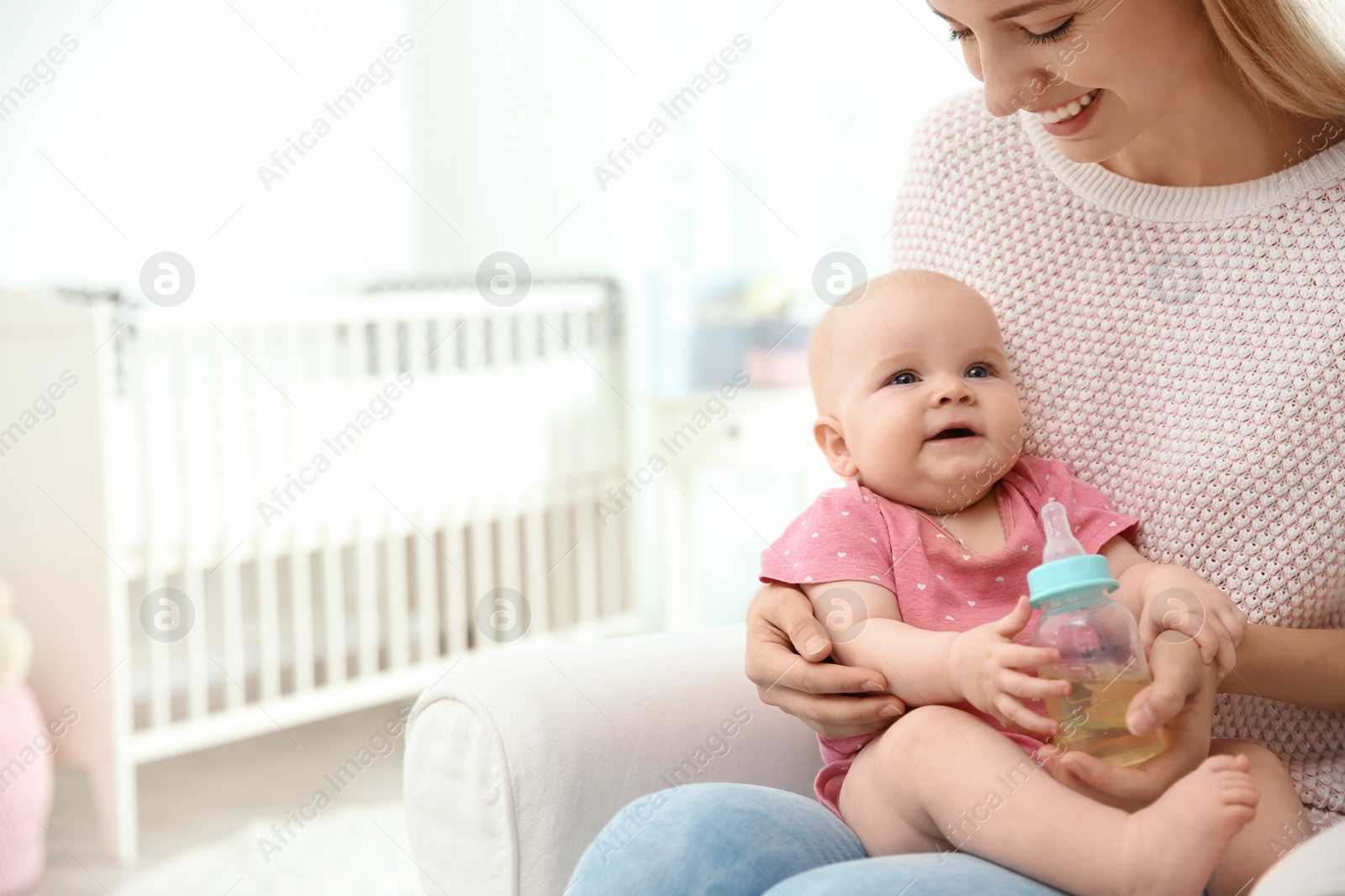 Photo of Lovely mother giving her baby drink from bottle in room. Space for text