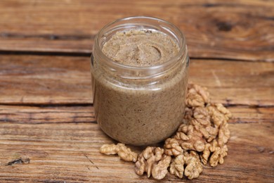 Tasty nut paste in jar and walnuts on wooden table, closeup