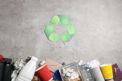 Photo of Recycling symbol and different garbage on gray background, top view